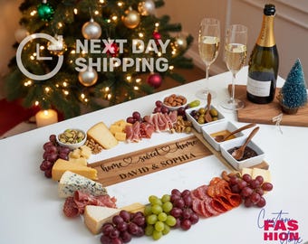 May include: A heart-shaped charcuterie board with cheese, meats, grapes, nuts, and olives. Includes a bottle of champagne and two glasses. The board is engraved with "home sweet home" and names. A Christmas tree is in the background.