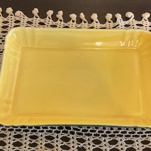 May include: A rectangular yellow ceramic serving dish with a scalloped edge. The dish has a smooth, glossy finish and a slightly raised rim. The dish is approximately 12 inches long and 8 inches wide.