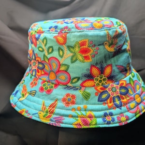 May include: A turquoise blue bucket hat with a colourful floral and hummingbird print. The flowers are made of beaded embroidery.