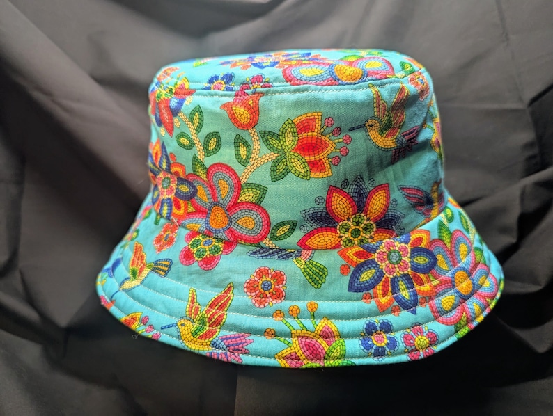 May include: A turquoise blue bucket hat with a colourful floral and hummingbird print. The flowers are made of beaded embroidery.