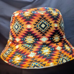May include: A bucket hat featuring a geometric pattern in shades of orange, red, yellow, blue, and black. The pattern is reminiscent of Native American designs.
