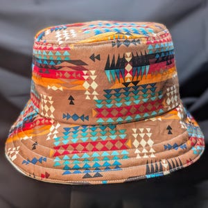 May include: A brown bucket hat with a colourful geometric pattern featuring triangles, diamonds and zigzags in shades of red, blue, yellow and white.