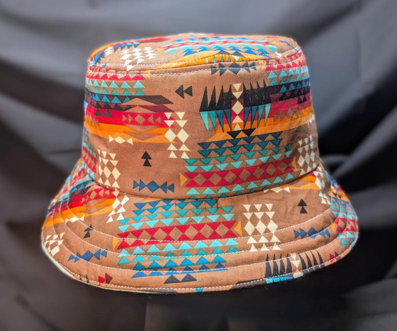 May include: A brown bucket hat with a colourful geometric pattern featuring triangles, diamonds and zigzags in shades of red, blue, yellow and white.