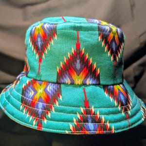 May include: A turquoise blue bucket hat with a colourful geometric pattern. The pattern features red, yellow, blue, white and black colours.
