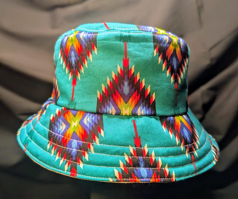 May include: A turquoise blue bucket hat with a colourful geometric pattern. The pattern features red, yellow, blue, white and black colours.