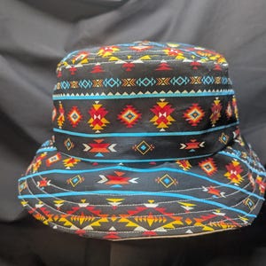 May include: A black bucket hat with a colourful geometric pattern in shades of red, yellow, blue, and white. The pattern is reminiscent of Native American designs.