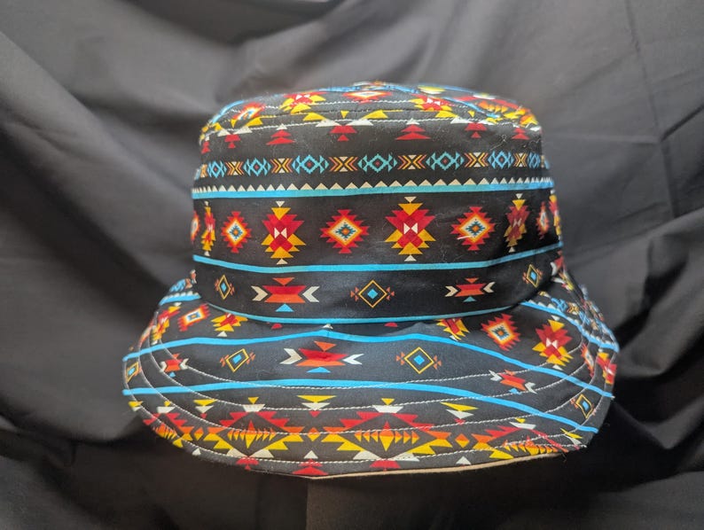 May include: A black bucket hat with a colourful geometric pattern in shades of red, yellow, blue, and white. The pattern is reminiscent of Native American designs.