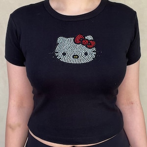 May include: Black short-sleeved t-shirt with a rhinestone Hello Kitty design. The bow is red.