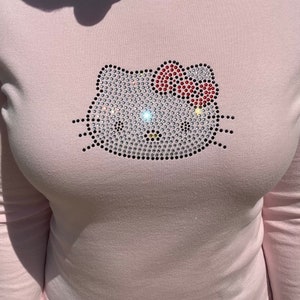 May include: A pink long-sleeved shirt with a rhinestone Hello Kitty design.