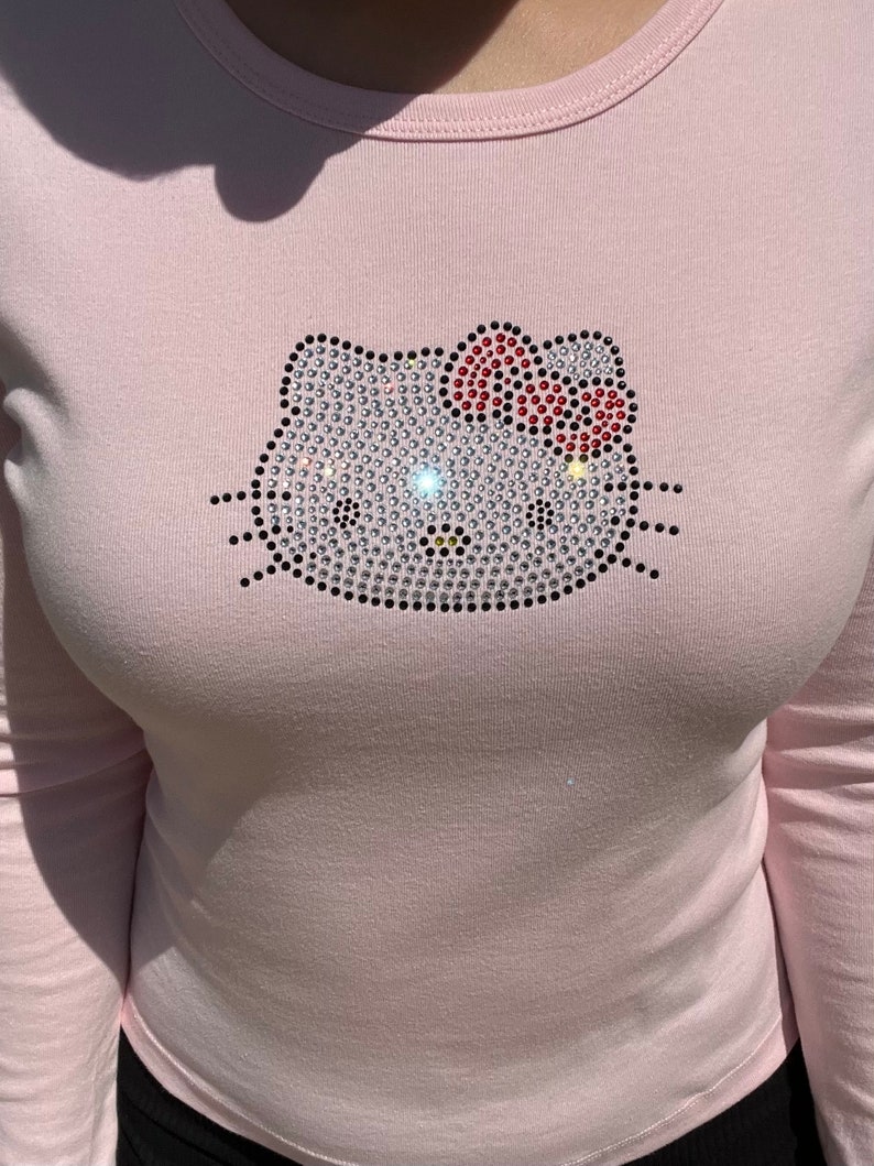May include: A pink long-sleeved shirt with a rhinestone Hello Kitty design.