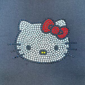 May include: A black t-shirt with a white Hello Kitty design made of rhinestones. The bow on Hello Kitty's head is red and white.
