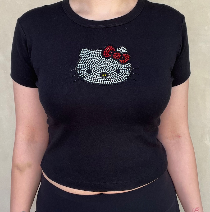 May include: Black short-sleeved t-shirt with a rhinestone Hello Kitty design. The bow is red.