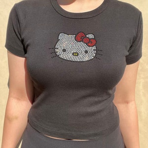 May include: Black short-sleeved t-shirt with a rhinestone Hello Kitty design. The bow on Hello Kitty is red.