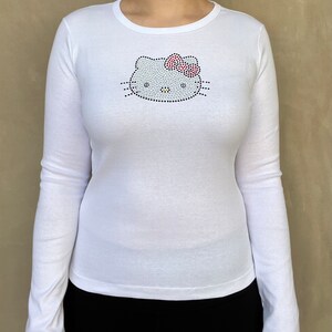 May include: White long-sleeved shirt with a rhinestone Hello Kitty design on the front.
