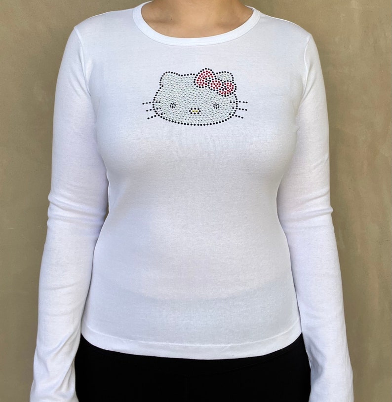 May include: White long-sleeved shirt with a rhinestone Hello Kitty design on the front.