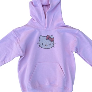Puede incluir: Una sudadera con capucha rosa claro con un dise&ntilde;o de Hello Kitty de diamantes de imitaci&oacute;n. La sudadera tiene un bolsillo canguro y una capucha con cord&oacute;n.