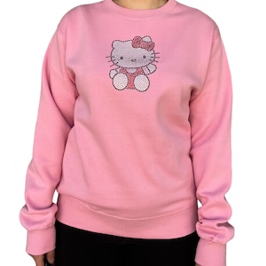 K&ouml;nnte beinhalten: Ein rosa Sweatshirt mit einem Hello Kitty-Motiv aus Strasssteinen.
