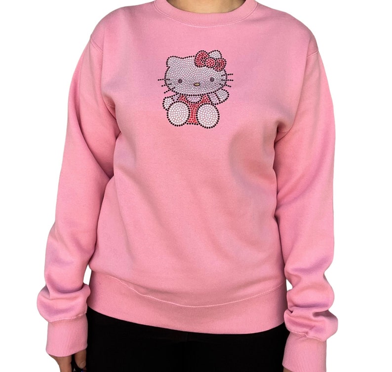 K&ouml;nnte beinhalten: Ein rosa Sweatshirt mit einem Hello Kitty-Motiv aus Strasssteinen.