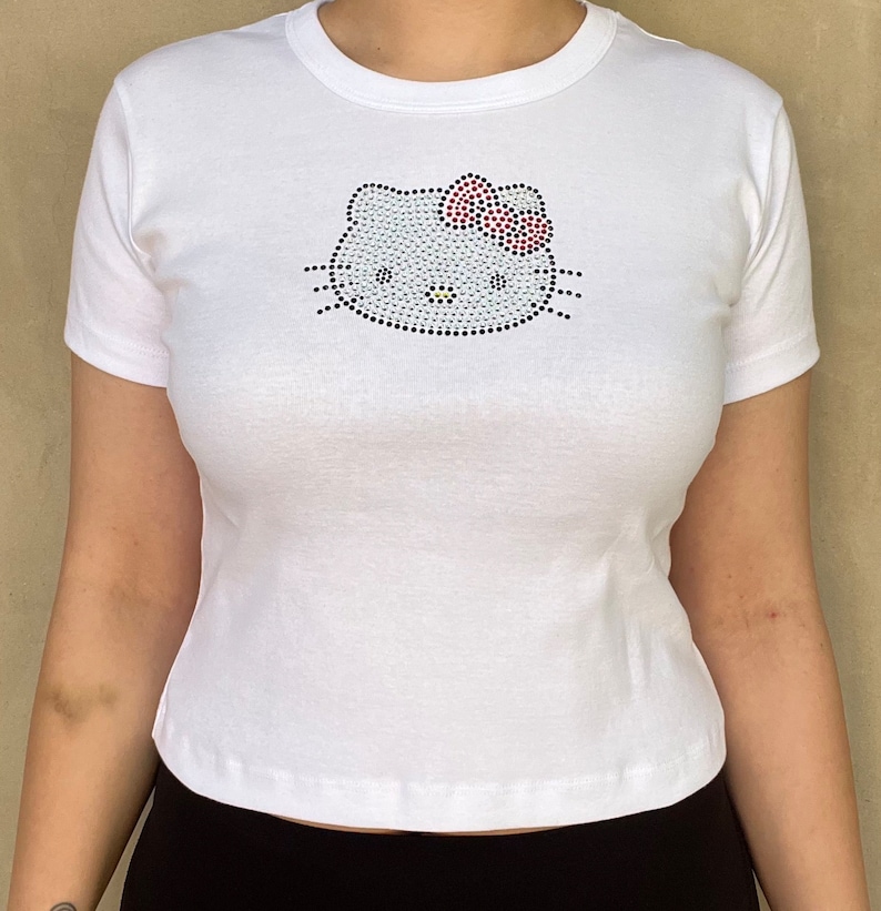 Pu&ograve; includere: Maglietta bianca con un design Hello Kitty in strass.