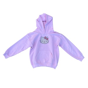 Puede incluir: Una sudadera con capucha rosa claro con un dise&ntilde;o de Hello Kitty de diamantes de imitaci&oacute;n en la parte delantera.