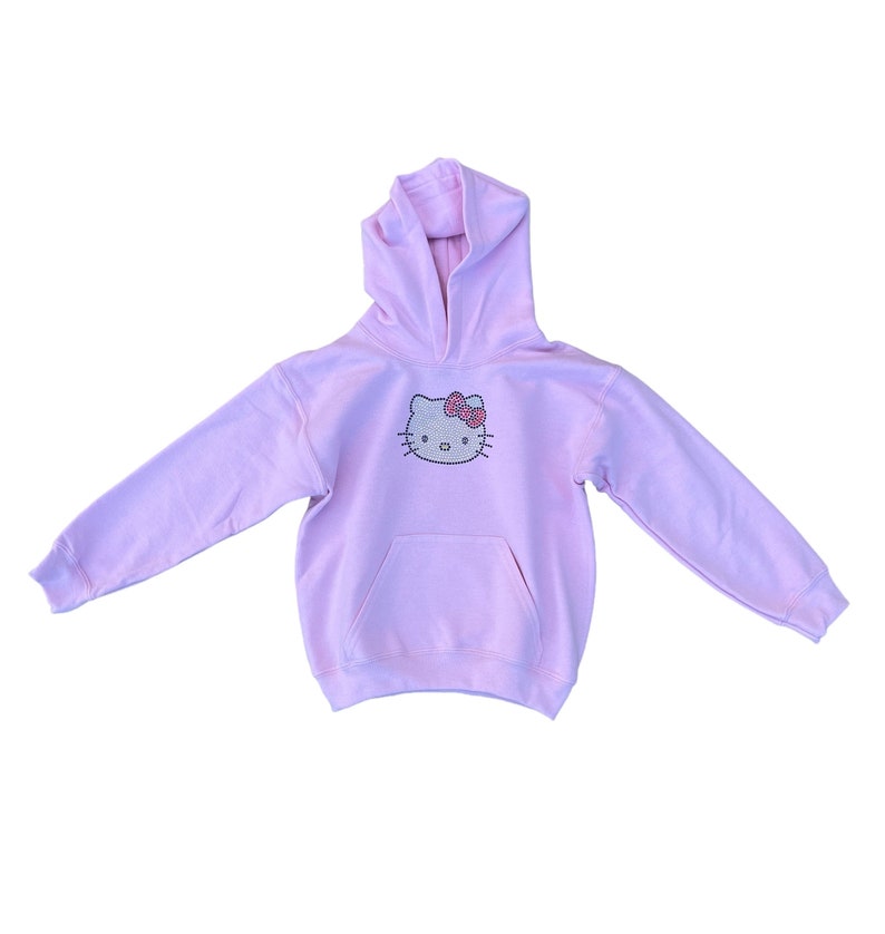 Puede incluir: Una sudadera con capucha rosa claro con un dise&ntilde;o de Hello Kitty de diamantes de imitaci&oacute;n en la parte delantera.