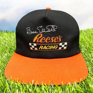 May include: Black and orange baseball cap with the text "Reese's Racing" and "Dale Earnhardt Jr." embroidered on the front.