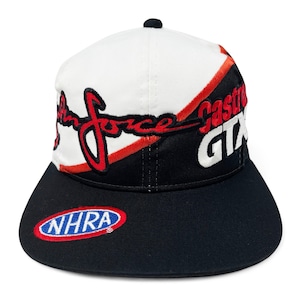 May include: A black and white baseball cap with red accents. The cap features the text "John Force" in red script, "Castrol GTX" in white, and an "NHRA" logo. The cap has a curved bill and a black button on top.
