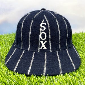 Könnte beinhalten: Eine marineblaue Baseballkappe mit weißen Nadelstreifen und dem Wort "SOX" in weiß auf der Vorderseite gestickt.
