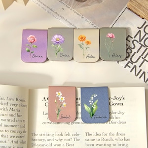 Könnte beinhalten: Sechs rechteckige magnetische Lesezeichen in verschiedenen Farben, jedes mit einer individuellen Blumenillustration und einem aufgedruckten Namen. Die Lesezeichen zeigen die Namen Edwina, Declan, Aiden, Hilary, Isabel und Frederica neben Blumenmotiven.
