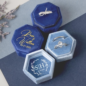 Può includere: Quattro scatole portaanelli in velluto blu. Due scatole sono blu scuro, una con i nomi "Rose & Walton" e la data "09-27-2025" in oro. Le altre due sono azzurre, una con le iniziali "S|H" e la data "06.20.2026".