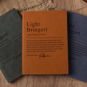 Puede incluir: Tres cuadernos en tonos verde, naranja y azul se muestran sobre una superficie de madera. Cada cuaderno presenta el texto "Light Bringert" con una definición. También se ven un bolígrafo y una tarjeta de "Thank You".