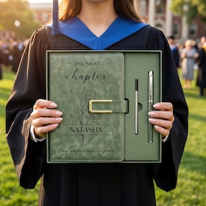 Puede incluir: Un juego de diario y bolígrafo verde con el texto "The Next Chapter" y el nombre "Natasha". El diario presenta un diseño floral y un cierre dorado. El juego incluye un bolígrafo y una recarga de bolígrafo.