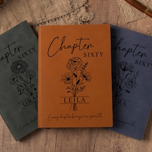 May include: Three personalised journals in grey, orange, and blue. Each cover displays "Chapter Sixty" in script, a floral design, and a name. The bottom of each journal reads "Every chapter brings new growth". The journals are on a wooden surface.