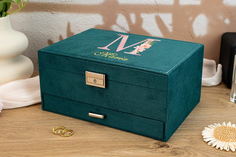 May include: A teal velvet jewelry box with a floral monogram and a lock. The box has a drawer and is perfect for storing jewelry.