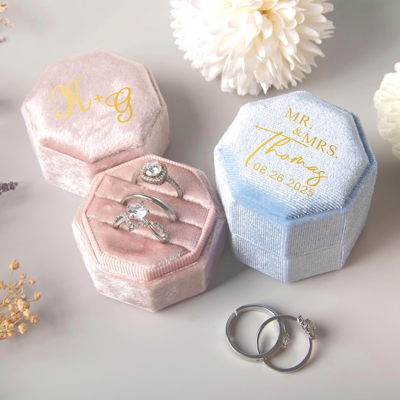 May include: Three velvet ring boxes in pink and blue, with gold lettering and rings. One pink box has the initials "H & G", another pink box holds two rings, and the blue box is inscribed "MR. & MRS. Thomas 08.26.2025".