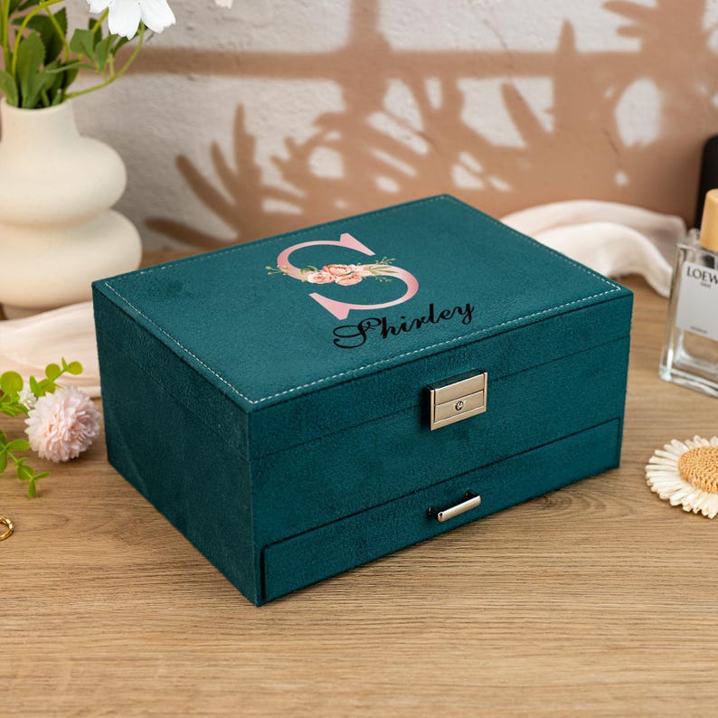 May include: Teal velvet jewelry box with a floral initial "S" and the name "Shirley" printed on the lid. The box has a hinged lid and a pull-out drawer.