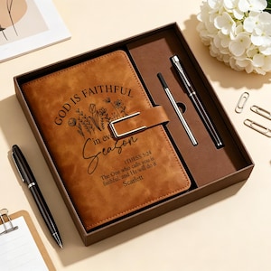 Könnte beinhalten: Ein beigefarbenes Notizbuch in Lederoptik mit Magnetverschluss, bedruckt mit dem Text "GOD IS FAITHFUL in every Season 1THESS 5:24 The One who calls you is faithful, and He will do it Scarlett" und Blumenmotiven, in einer Box mit zwei Stiften.