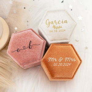 Könnte beinhalten: Drei sechseckige Ringboxen mit Samt-Innenausstattung. Die Boxen sind in Beige, Rosa und Orange. Die beige Box hat den Text "Garcia 04.18.2024" auf der Oberseite. Die rosa Box hat den Text "e♥k" auf der Oberseite. Die orange Box hat den Text "Mr & Mrs 05.20.2024" auf der Oberseite.