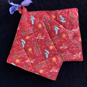 May include: Two red quilted pot holders with a white and green pattern. The pattern features the text "All I Want For Christmas" and a wand, socks, and stars.