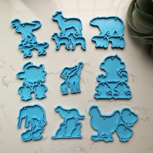 Könnte beinhalten: Neun blaue Silikonformen zum Backen von tierförmigen Kuchen. Jede Form zeigt ein anderes Tier, darunter eine Giraffe, eine Schildkröte, ein Huhn, ein Bär, ein Elefant, ein Hund und ein Dinosaurier, wobei jedes Tier eine kleinere Version von sich selbst hat.