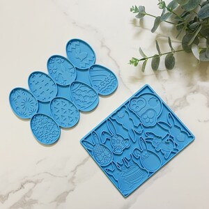 Könnte beinhalten: Zwei blaue Silikonformen zum Backen. Eine Form hat acht Oster-Eiformate, die andere hat acht Hasenformen.