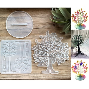 Può includere: Uno stampo in silicone trasparente per realizzare un porta gioielli a forma di albero. Lo stampo è composto da tre pezzi: una base, un tronco e una cima d'albero. Lo stampo è mostrato su una superficie di legno con esempi di porta gioielli finiti.