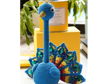 May include: A blue crocheted peacock with a colorful tail and jeweled accents. The peacock has a long neck and a small, round body.