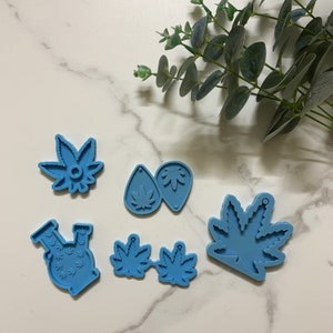 Puede incluir: Un juego de seis moldes de silicona azul para hacer pendientes de resina y otras manualidades. Los moldes presentan varios diseños, incluyendo una hoja de marihuana, una pipa de agua y una forma de lágrima.
