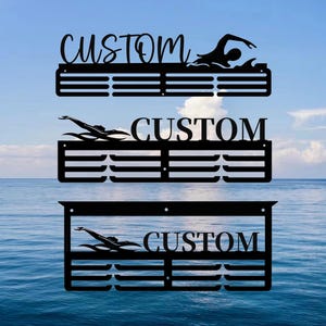 Peut inclure: Trois supports de médailles en métal noir avec une silhouette de nageur et le mot "CUSTOM" sur chacun. Les supports ont 10 emplacements pour les médailles.