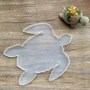 Puede incluir: Un molde de silicona transparente con forma de tortuga. El molde está sobre una superficie de madera.