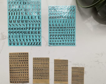 May include: Six sheets of alphabet stickers with black letters on a light blue and beige background. The letters are in uppercase and include A through Z.