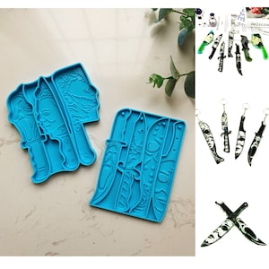 Könnte beinhalten: Zwei blaue Silikonformen zum Herstellen von Kunsthandwerk aus Harz. Eine Form zeigt einen Stapel Messer mit einem Totenkopfdesign. Die andere Form zeigt drei verschiedene Messerdesigns mit einem Totenkopfdesign.
