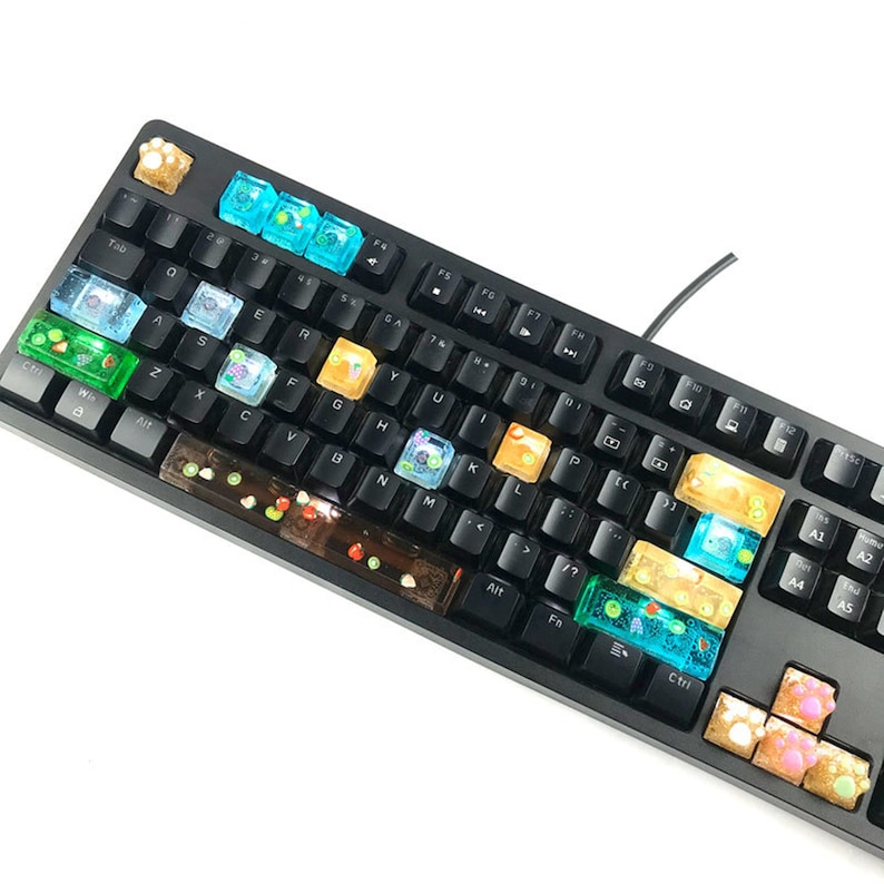 May include: Black mechanical keyboard with custom keycaps. The keycaps are transparent with colorful designs, including fruit, bubbles, and other decorative elements. The keyboard has a standard layout with a wired connection.