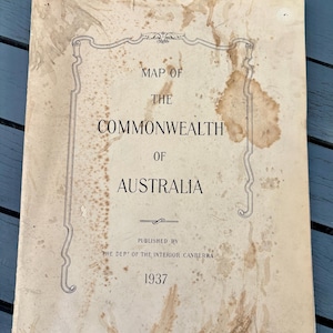 Puede incluir: Un mapa antiguo de Australia de 1937, titulado "Map of the Commonwealth of Australia". La portada está envejecida con manchas y presenta un borde ornamentado. Publicado por The Dept of the Interior Canberra.